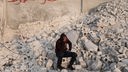 15-Jähriger in Kapuzenpuillover sitzt auf Trümmern und stützt den Kopf in der Hand