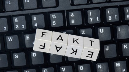 Auf einer Tastatur liegen Würfel mit Buchstaben, die auf einer Seite das Wort "Fake", auf der anderen Seite das Wort "Fakt" zeigen