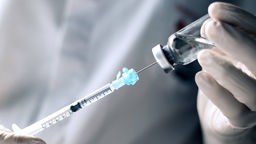 Hände mit Einmal-Handschuhen ziehen eine Nadel mit Impfstoff auf