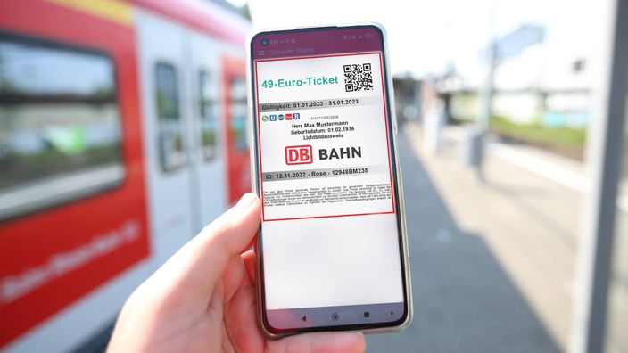 Hand hält Smartphone auf dem ein Bahnticket mit der Überschrift "49-Euro-Ticket" zu sehen ist
