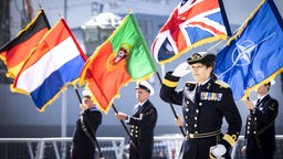 Commander Jeannette Morang salutiert vor Flaggen der Nato und Bündnisstaaten