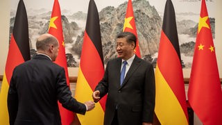 Scholz geht auf Xi Jinping zu, der vor deutschen und chinesischen Flaggen steht