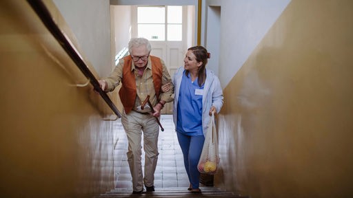 Lächelnde Pflegerin hilft einem Senior beim Treppensteigen.