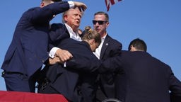 Mitarbeiter des Secret Service stehen schützend um Trump, der mit Blut an Ohr und Wange am Rednerpult steht