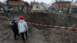 Zwie Kinder stehen in der Ukraine vor einem Krater.