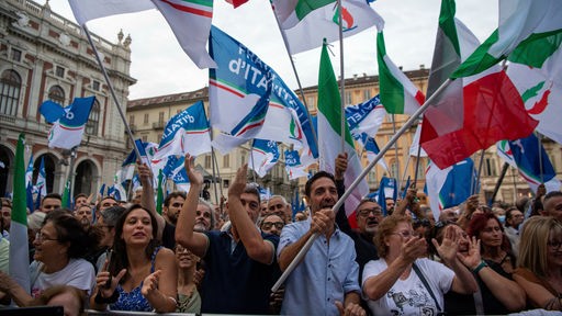Menschen auf einem Platz schwenken italienische Fahnen und Fahnen der Partei Fratelli d'Italia