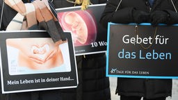 Mit Plakaten mit der Aufschrift "Mein Leben ist in deiner Hand..." und "Gebet für das Leben" und dem Bild eines 10 Wochen alten Embryo demonstrieren Abtreibungsgegner:innen vor der Beratungsstelle von Pro Familia.