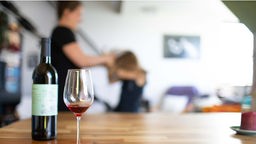 Symbolbild: Im Vordergrund eine Flasche Wein, im Hintergrund eine Erwachsene, die ein Kind schlägt.