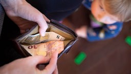 Kind schaut hoch zu einem Elternteil mit Geldbörse in der Hand