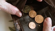 Symbolbild: Älterer Mensch hält Geldbörse in der Hand, die nur noch Münzen enthält