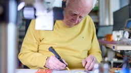 Älterer Mann arbeitet in einer Werkstatt an einer Platine (Symbolbild)