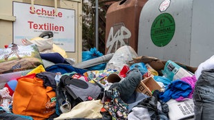 Berge von Altkleidern vor Sammelcontainern