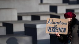 Eine Frau hält ein Schild mit der Aufschrift "Antisemitismus ist Verbrechen" neben einer Stele vom Holocaust Mahnmal, Archivbild: 27.01.2021