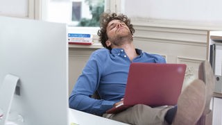 Mann schläft mit Laptop auf dem Schoß. Symbolbild