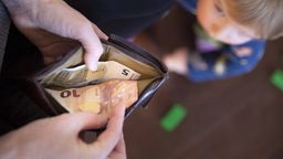 Blick in eine geöffnete Geldbörse mit nur 15 Euro, im Hintergrund ein kleines Kind