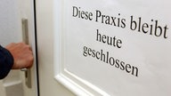 Ein Mann versucht die Tür einer geschlossenen Arztpraxis zu öffnen.