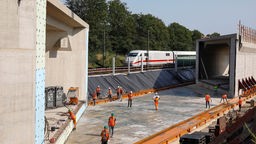 Arbeiter verbreitern im Auftrag der Deutschen Bahn die Schienentrasse in Bonn-Vilich, im Hintergrund rollt ein ICE vorbei. 