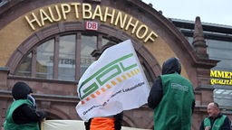 Gewerkschaftsmitglieder stehen mit Fahne und Transparent vor dem Erfurter Hauptbahnhof. Archivbild: 24.01.2024