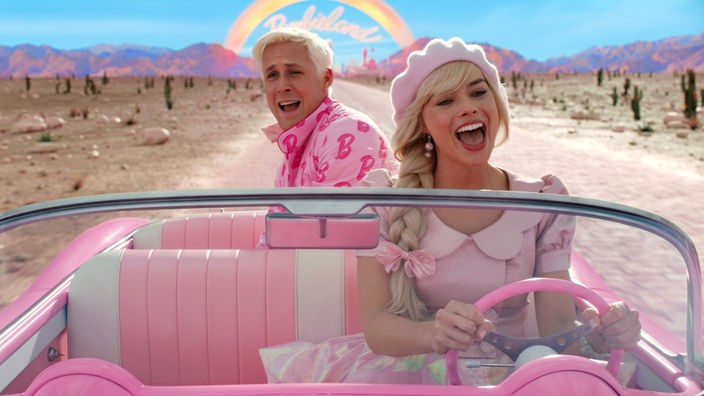 Filmszene: Barbie (Margot Robbie) und Ken (Ryan Gosling) in einem rosa Cabrio.