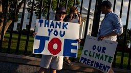 Vor dem Weißen Haus in Washington stehen zwei Menschen mit Plakaten "Thank You Joe" und "Our Climate President" (21.07.2024)