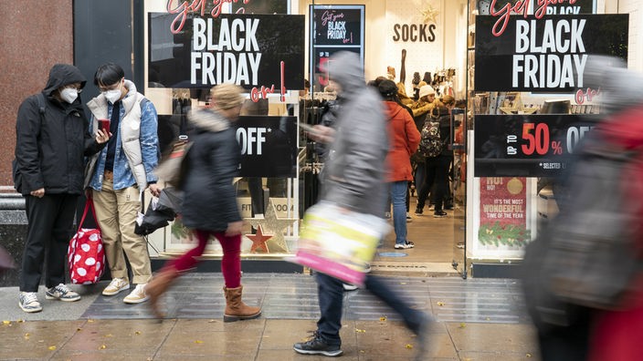 Passanten gehen an einem Geschäft vorbei mit Werbung an der Scheibe für Black Friday 