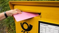 Symbolbild: Ein Umschlag zur Briefwahl wird in einen gelben Briefkasten eingworfen