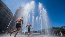 Symbolbild: Zwei Menschen gehen durch Wasserfontänen auf einem Platz in Frankfurt am Main.