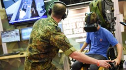 Symbolbild: Ein Kind sitzt bei der Computerspielemesse "Gamescom" 2018 auf dem Stand der Bundeswehr auf dem Sitz eines Tornado und wird von einem Soldaten angeleitet. 