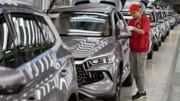 Chinesischer Mitarbeiter entfernt Klebestreifen von den einer Reihe von neuen Autos in einem Werk