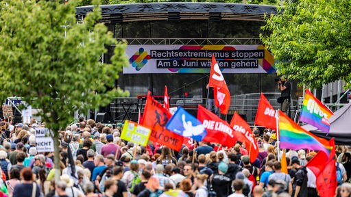 Demonstrierende mit Fahnen vor einer Bühne mit einem Plakat mit dem Text "Rechtsextremismus stoppen. Am 9. Juni wählen gehen!"