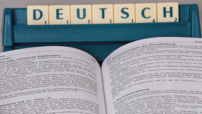 Ein aufgeschlagener Duden liegt vor dem aus Scrabble-Buchstaben gebildeten Wort "Deutsch"
