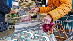 Kundin packt an der Supermarktkasse Mineralwasser, Zwiebeln und Fleisch in den Einkaufwagen