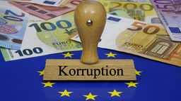 Ein Stempel mit der Aufschrift "Korruption" steht auf der EU-Flagge. Im Hintergrund Geldscheine (Symbolbild)