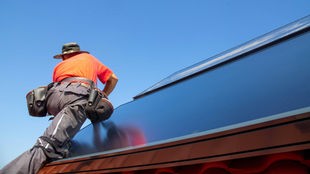 Symbolbild: Ein Mensch montiert eine Solaranlage auf einem Dach
