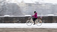 Eine Frau fährt mit ihrem Fahrrad über einen verschneite Brücke