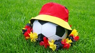 Symbolbild: Ein Fußball mit Hut und Blumenkette in den deutschen Nationalfarben.