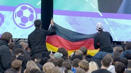 Fans halten eine Deutschlandfahne hoch in einer Fanzone der EM 2024 in Berlin