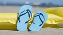 Blaue Flip-Flops und eine gelbe Luftmatratze am Strand. Symbolbild