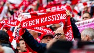 Fans des FC Köln halten rote Schals mit der Aufschrift "Gegen Rassismus - Nazis raus"