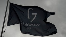 Schwarze Fahne mit einem Logo aus einem G und der Zahl 7 weht vor grauem Himmel