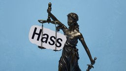 Justitita-Statue hält ein Schild mit der Aufschrift "Hass" in ihrer Wagschale