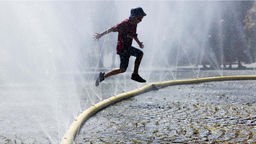 Ein Kind springt über einen perforierten Feuerwehrschlauch. Im Rahmen des Hitzeaktionsplans der Stadt Köln testet die Stadt 2022 Wasserschläuche gegen die Sommerhitze