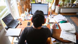 Ein Mensch sitzt mit Kopfhörer und Laptop an einem Schreibtisch im Homeoffice.