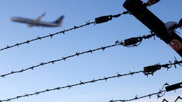 Ein Flugzeug fliegt über ein Gebäude mit Stacheldraht.