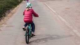 Symbolbild: Ein Kind in Jacke und mit Helm fährt Fahrrad.