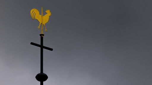 Symbolbild: Kreuz und Wetterhahn auf einem Kirchendach vor dunklen Wolken