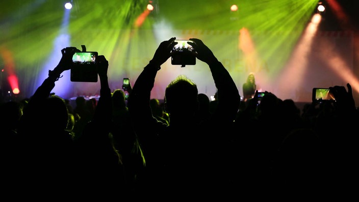 Symbolbild: Menschen nehmen mit ihren Smartphones den Auftritt einer Band während eines Konzerts auf.