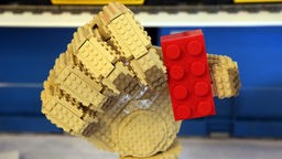 Eine aus gelben Legosteinen gebaute Hand hält einen roten Legostein
