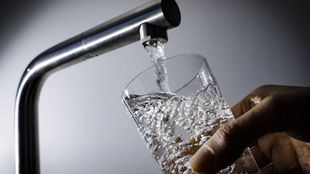 Wasser fließt aus einem Wasserhahn in ein Glas