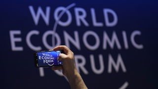 Eine Person macht mit dem Handy ein Foto vom Logo des Weltwirtschaftsforums (World Economic Forum)
